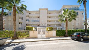Een hotel met meerdere verdiepingen, een centrale ingang, palmbomen en een heldere lucht.
