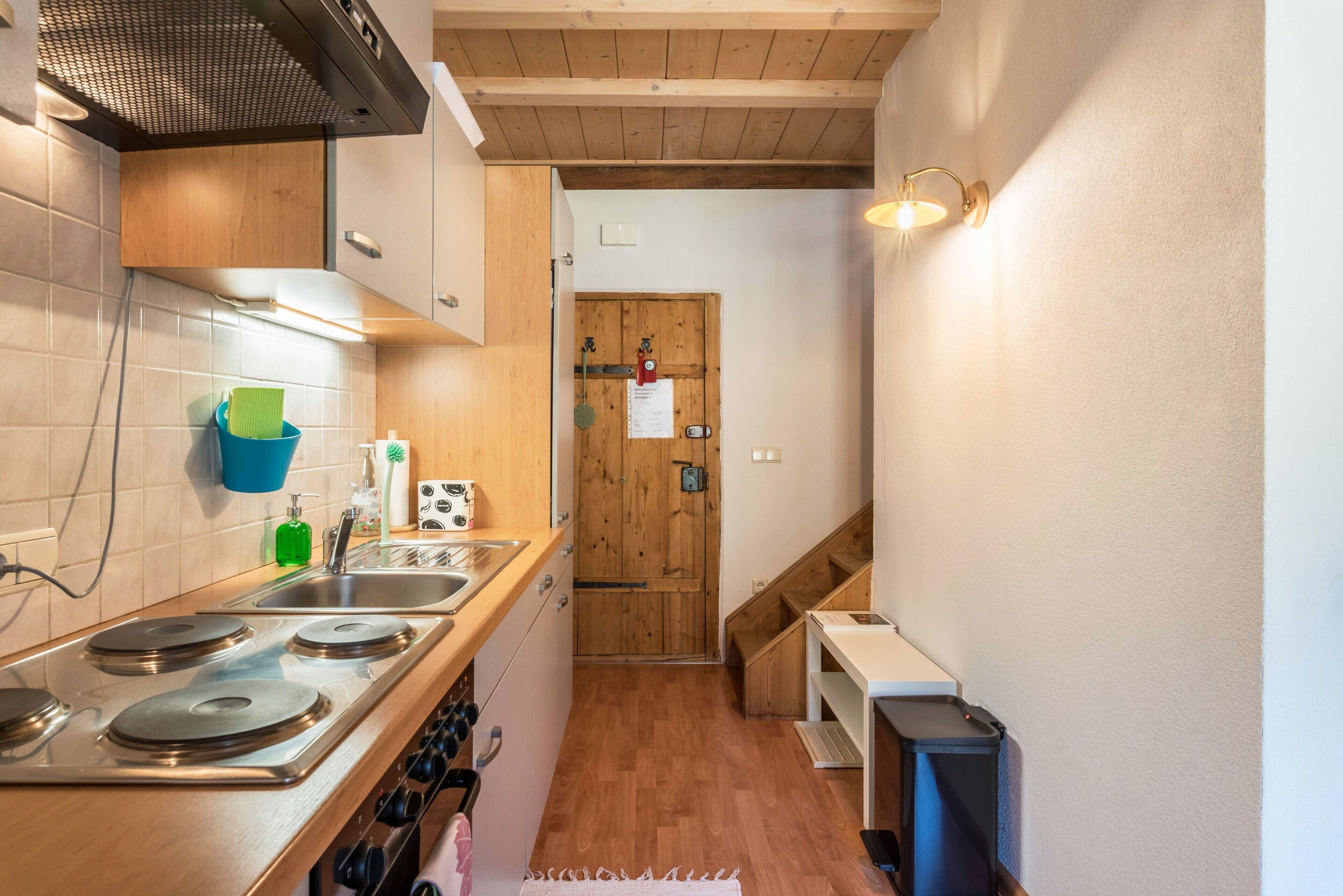 Una cucina compatta con piano di lavoro in legno, fornello in acciaio inossidabile e porta in legno.