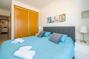 Un dormitorio con cama, mesita de noche, lámpara, armario y un cuadro en la pared.