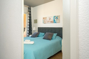 A bedroom with a bed, pillows, a wall-mounted artwork, and a door leading to another room.