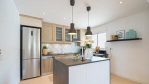 Une cuisine moderne dotée d’un réfrigérateur en acier inoxydable, de meubles en bois, d’un îlot central agrémenté d’un vase, de luminaires suspendus et d’un dosseret carrelé.