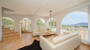 Un salon spacieux avec un canapé blanc, une table basse et un tapis noir. De grandes fenêtres en arc offrent une vue sur l’extérieur.