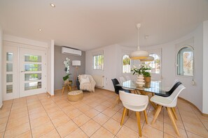 A spacious dining area with a glass table, white and black chairs, and a hanging pendant light.