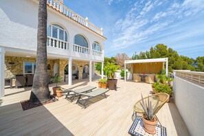 A spacious outdoor patio with a pool, lounge chairs, and potted plants.