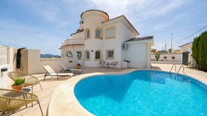 Un espace aménagé au bord de la piscine, comprenant une piscine, des chaises longues et un bâtiment au style architectural particulier.