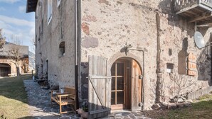 A rustic stone building with a wooden door, a bench, and a small garden area. - Studio 'Moserhof - Sunnseit' with Mountain View, Garden & Wi-Fi (Sarnthein)