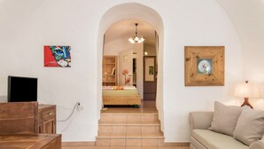 A room with a wooden desk, a sofa, a TV, a staircase leading to a bedroom, and a hallway with a wooden door. - Studio 'Moserhof - Sunnseit' with Mountain View, Garden & Wi-Fi (Sarnthein)