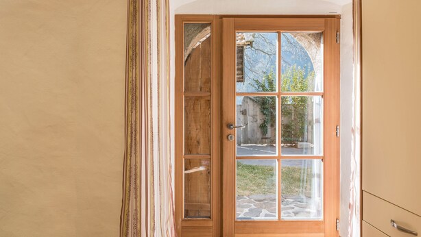A wooden door with glass panels, a metal handle, and a view of the outside. - Studio 'Moserhof - Sunnseit' with Mountain View, Garden & Wi-Fi (Sarnthein)