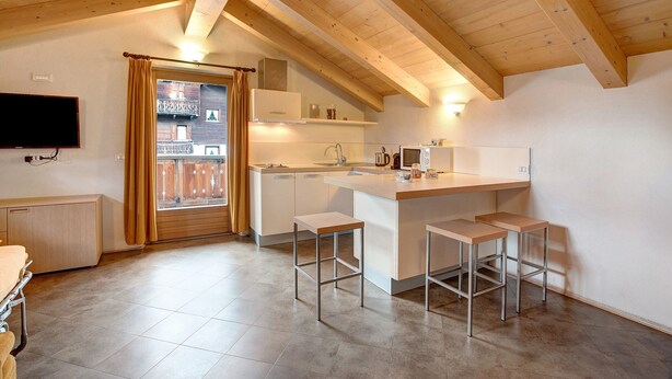 Una cucina moderna con soffitto in legno, piano cottura integrato, lavandino e sgabelli da bar.