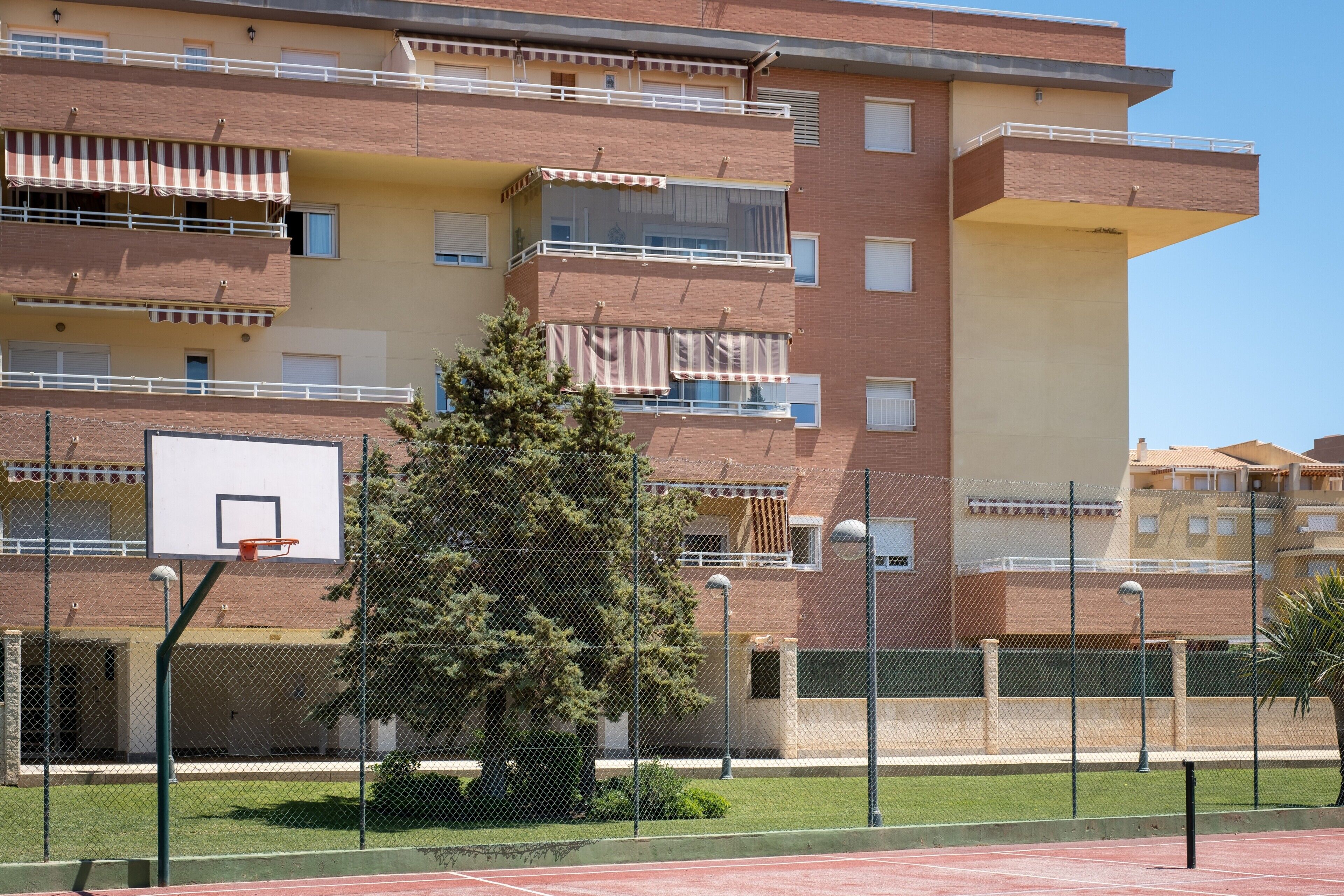 A multi-story residential building with balconies, a basketball court, and a fenced sports area.