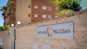 Ein Gebäude mit einem Schild, das 'MARINAS DE PROCUSAN' zeigt, und einer Steinmauer mit zwei Metalltüren.
