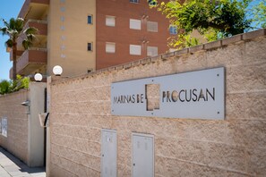 Un edificio con un cartel que dice 'MARINAS DE PROCUSAN' y un muro de piedra con dos puertas de metal.