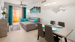 Ein modernes Wohnzimmer mit einem grauen Sofa, Türkis-Kissen und einem Essbereich mit Tisch für vier Personen.