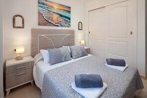 Un dormitorio ordenado con cama, lámparas de noche, mesita de noche y una puerta.