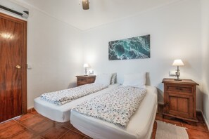 A bedroom with two beds, a wooden door, a wall-mounted air conditioner, a nightstand with a lamp, and a painting. - Holiday Home Casa Linda with Mountain View, Wi-Fi, A/C, Balcony & Terrace (Guaro)