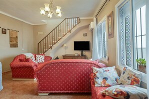 A room with a staircase, a TV, a sofa, and a window with patterned shutters. - Holiday Home Casa Linda with Mountain View, Wi-Fi, A/C, Balcony & Terrace (Guaro)