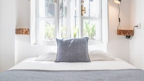 A neatly made bed with a patterned pillow, a window with white frames, and a wall-mounted lamp. - Las Brisas Estepona (Estepona)