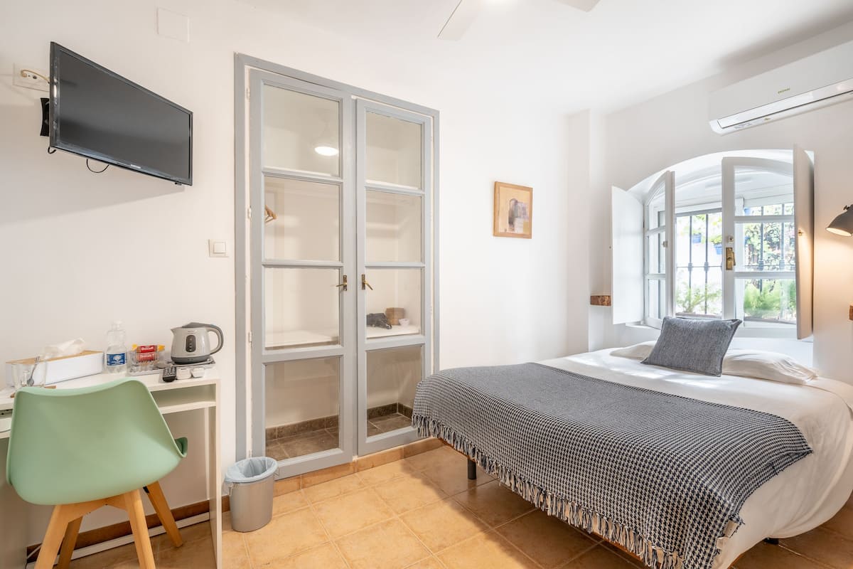 A bedroom with a bed, a desk with a chair, a television, a wardrobe, and a window with a view.