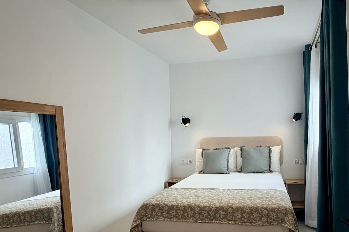 A bedroom with a bed, a ceiling fan, bedside lamps, and a window with curtains.