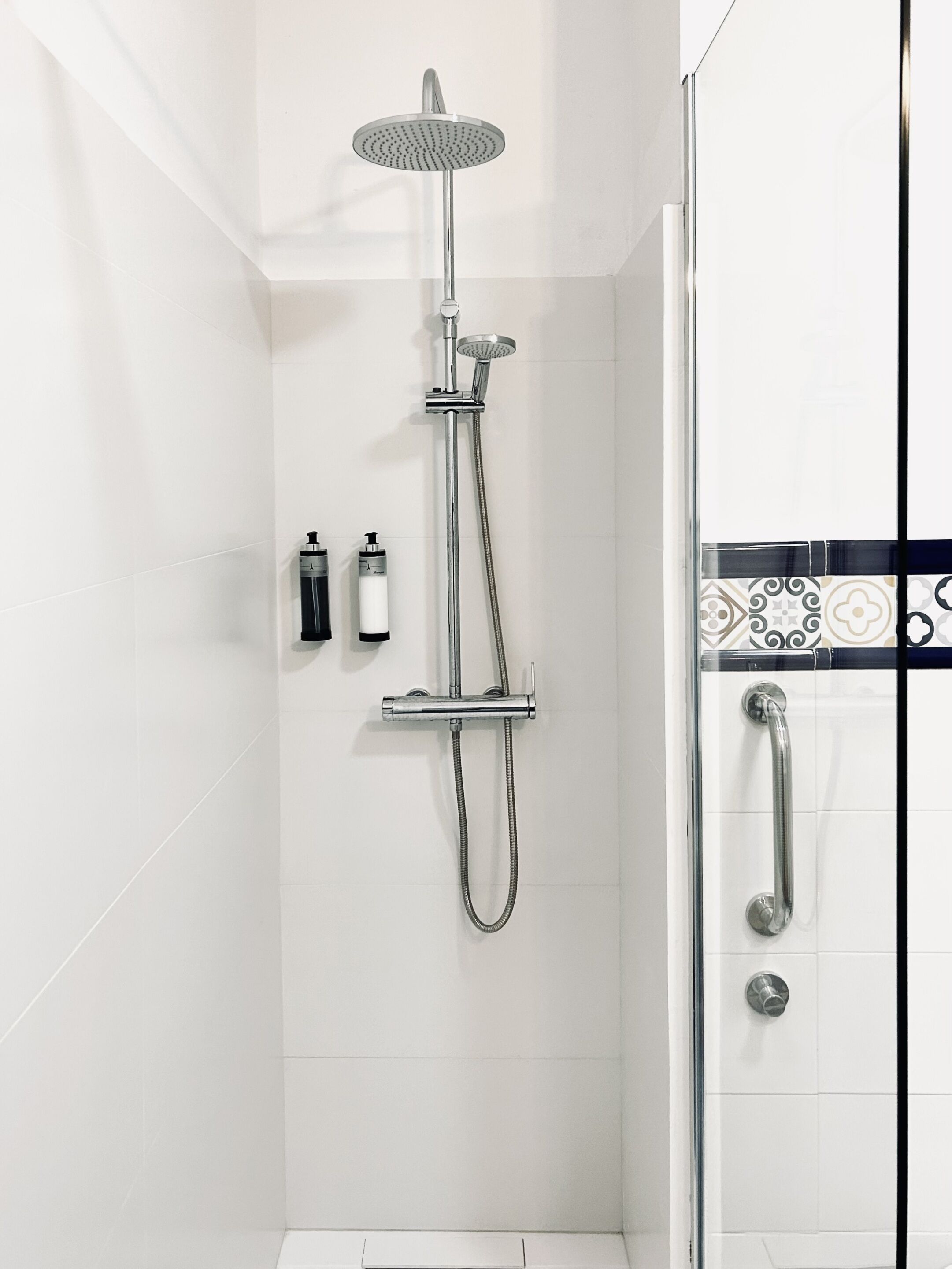 Eine moderne Dusche mit Handbrause und Deckenbrause, einer Duschkabine aus Glas und einem gefliesten Boden.