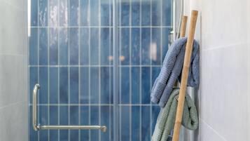 Un baño con mampara de vidrio, un perchero con toallas y un pasamanos.
