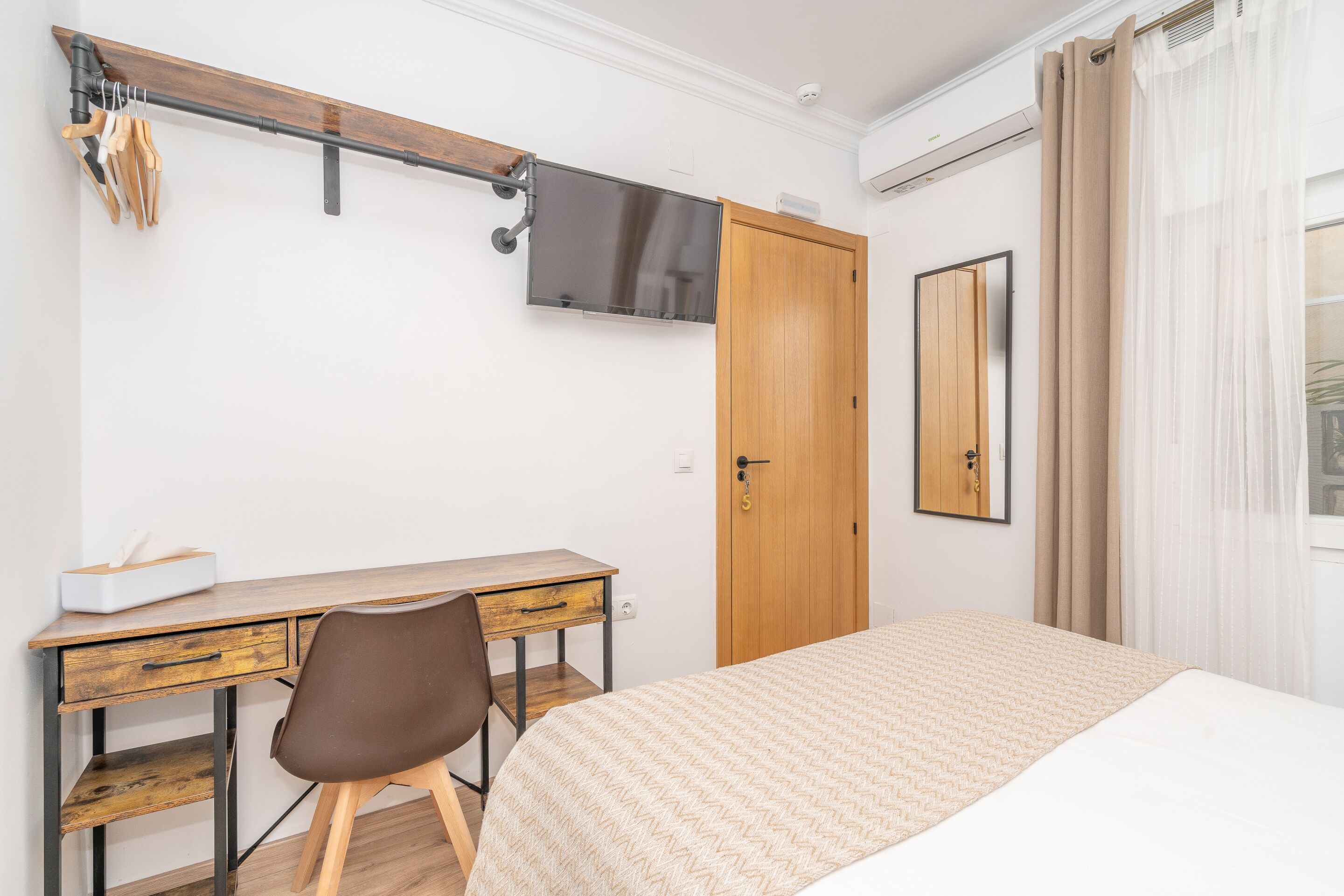 Une chambre à coucher comprenant un lit, un bureau, une chaise, un téléviseur fixé au mur et une porte.