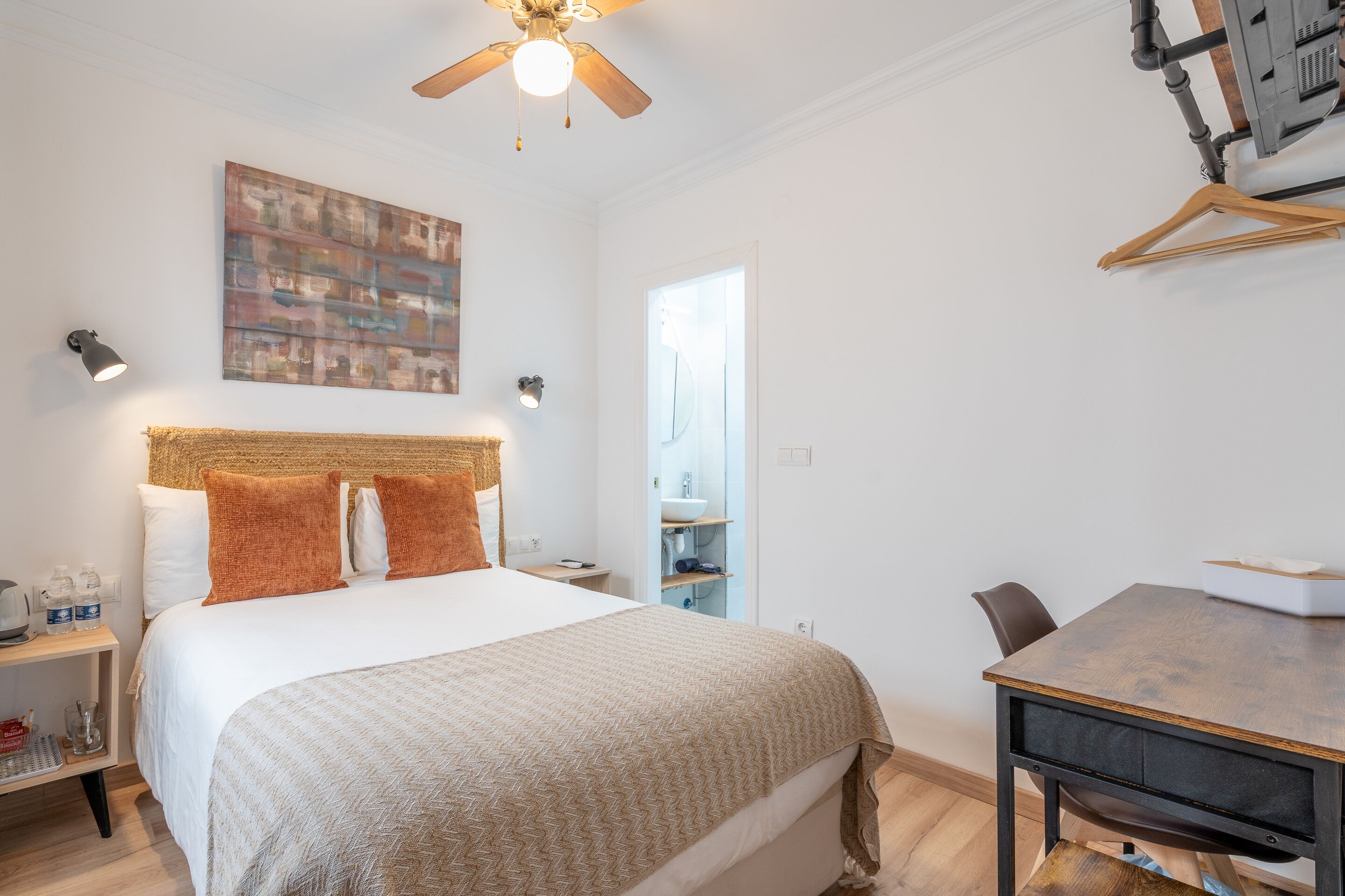 Ein Hotelzimmer mit Bett, Nachttisch, Lampe und Schreibtisch mit Stuhl.