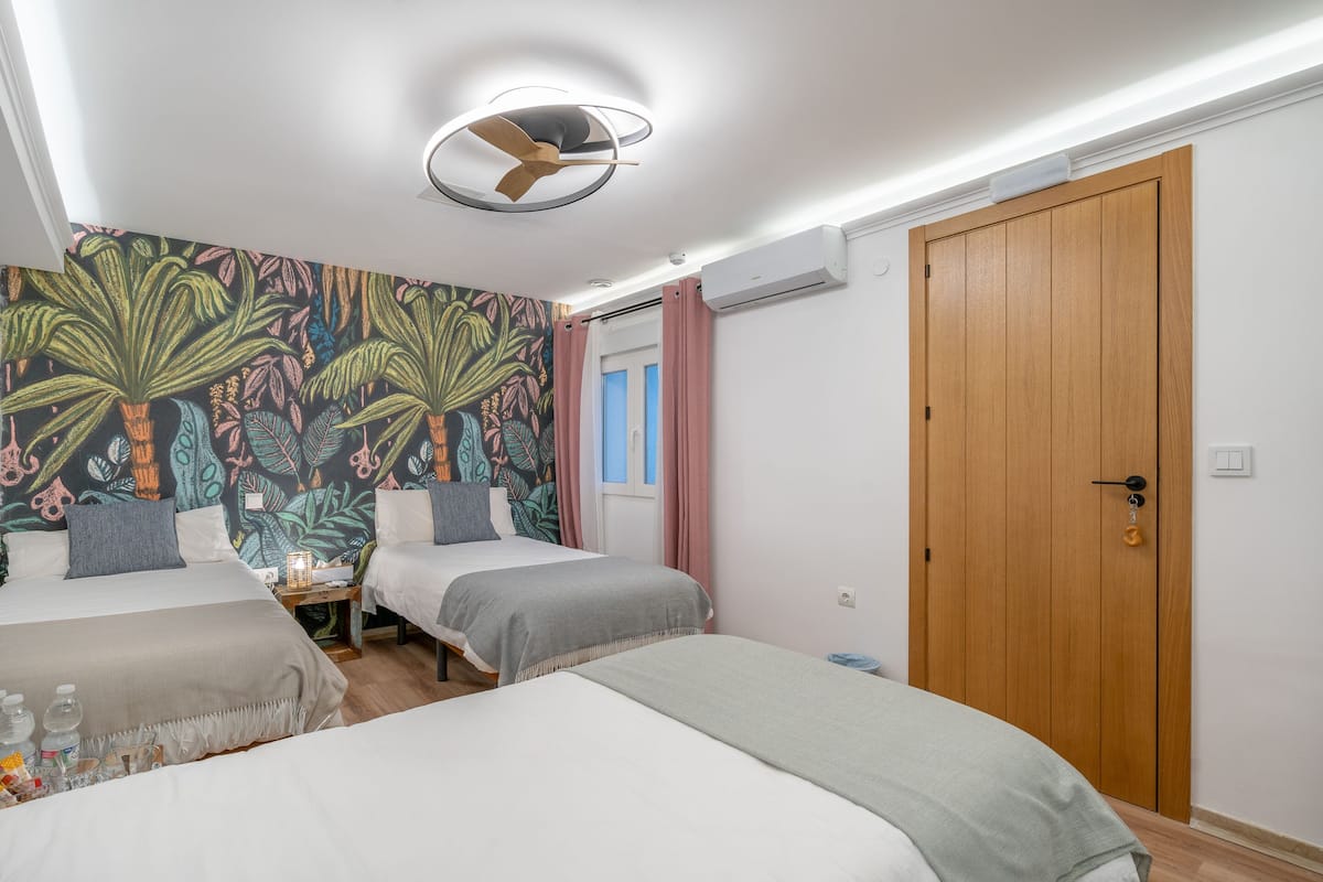 A hotel room with two beds, a ceiling fan, an air conditioning unit, and a door.