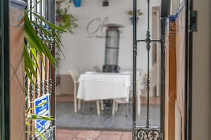 An open doorway leading to a dining area with a white tablecloth-covered table and chairs, a potted plant, and a wall with a sign.