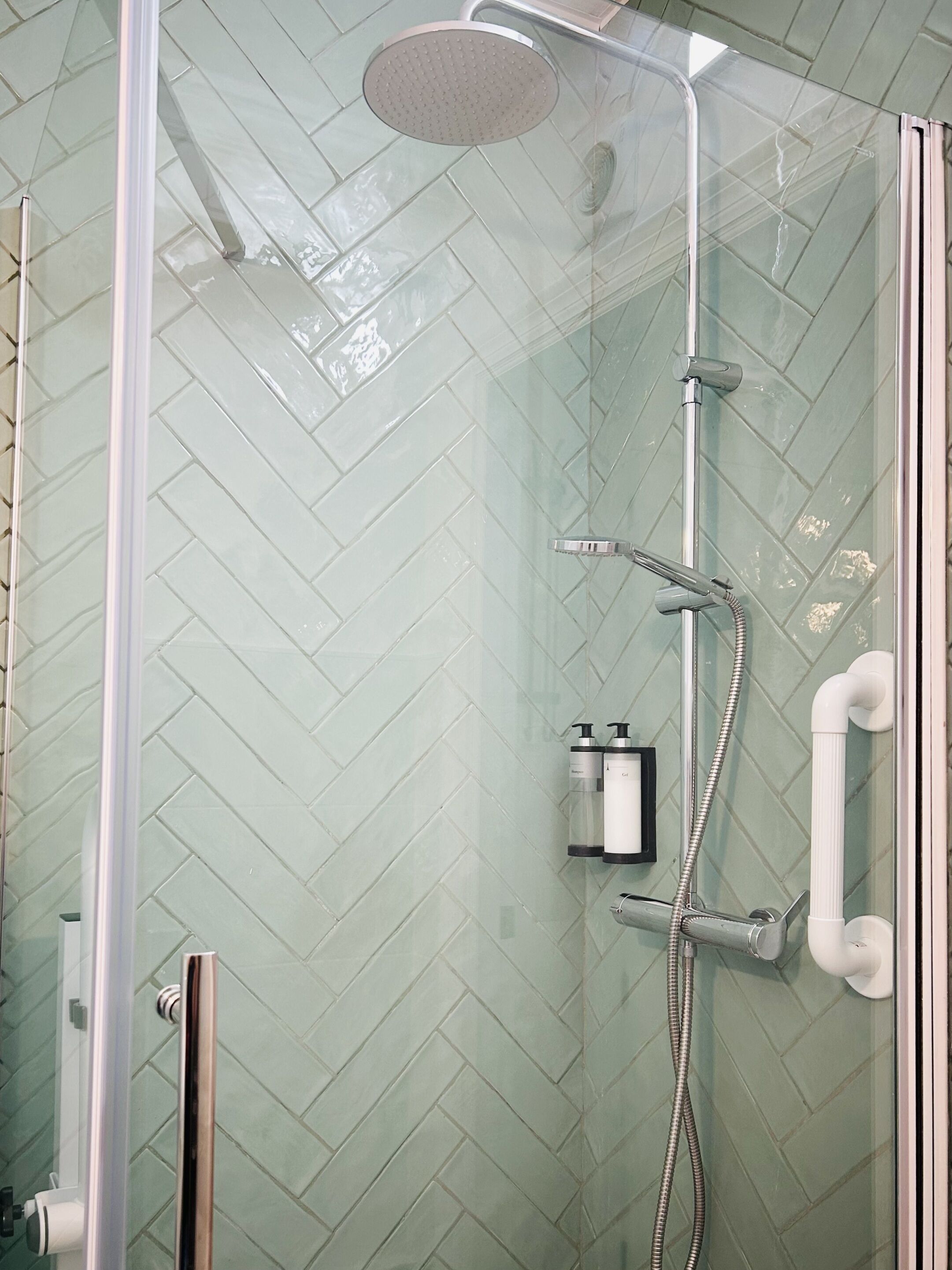 A glass-enclosed shower with a herringbone tile pattern on the walls.