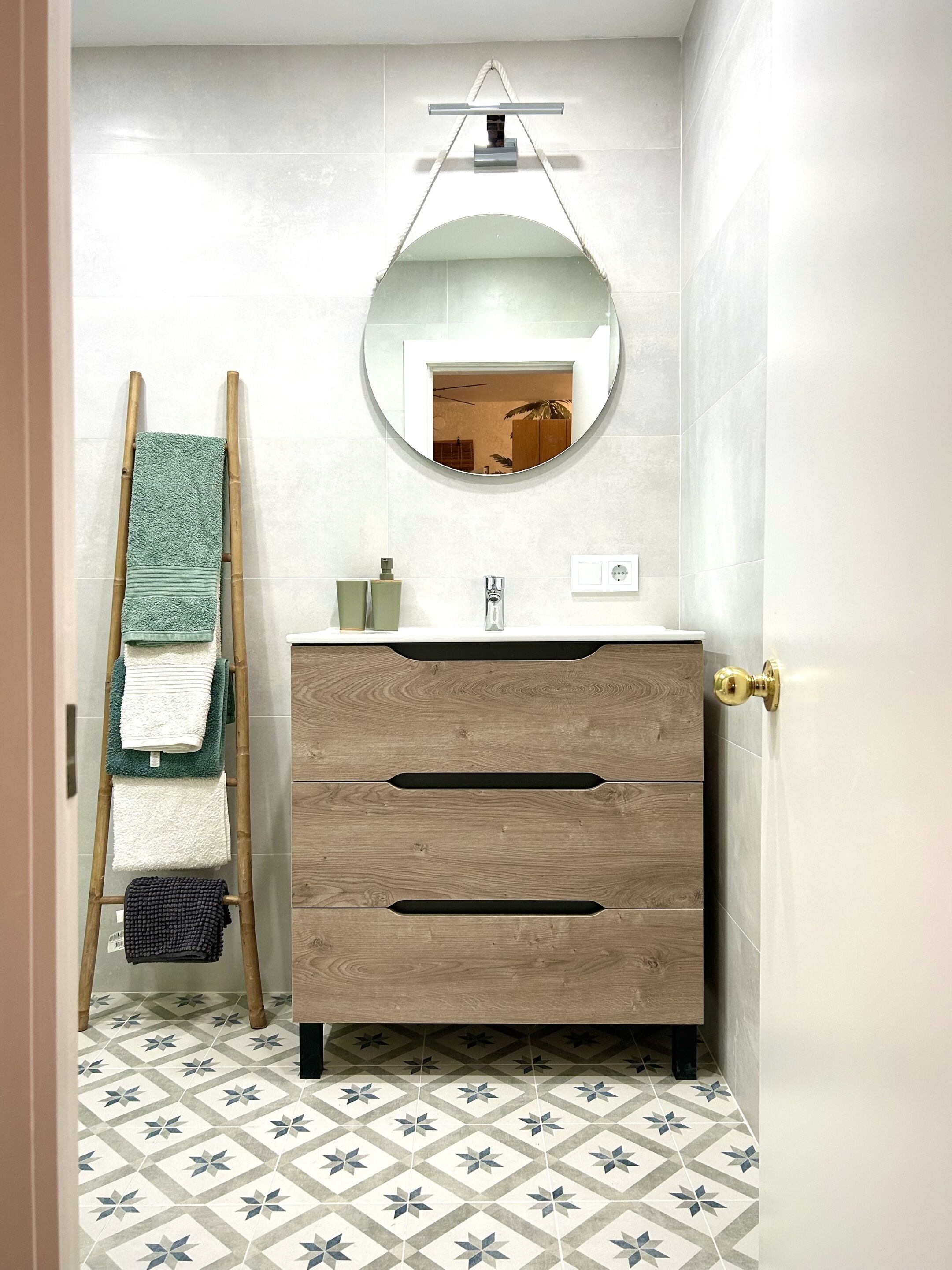 A bathroom with a wooden vanity, a round mirror, and a towel rack.