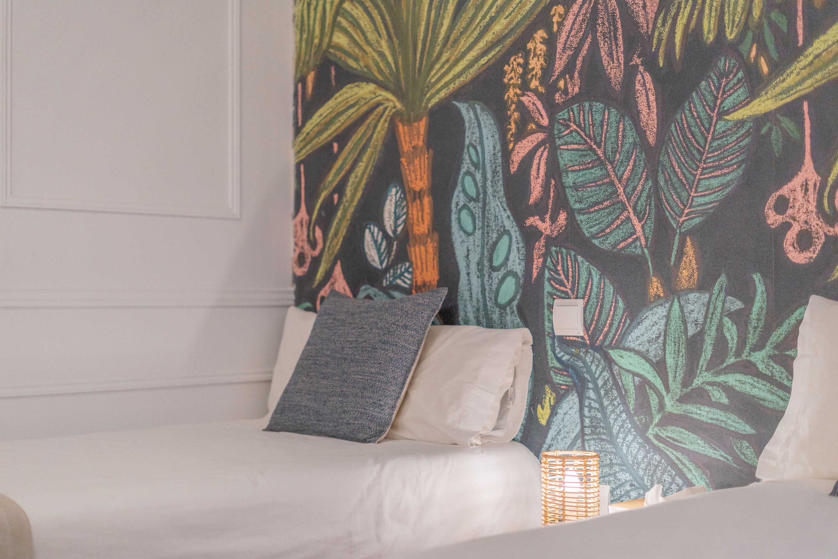 A bed with white bedding, a gray pillow, and a patterned wall behind it.