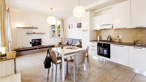 Une cuisine moderne avec des meubles blancs, une table à manger avec des chaises, un téléviseur et un canapé.