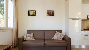 Un canapé en cuir marron agrémenté de deux coussins décoratifs, une fenêtre avec des rideaux et deux tableaux encadrés accrochés au mur.