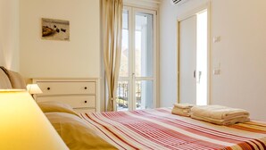 Une chambre à coucher avec un lit, une table de chevet, une lampe, une fenêtre avec des rideaux et un tableau au mur.