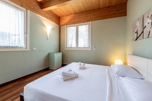 Camera da letto con due letti, travi in legno al soffitto, un termosifone e una finestra con tende.
