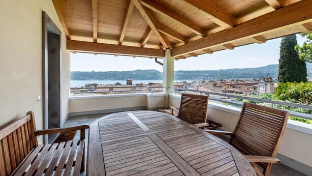 A wooden deck with a table and chairs, overlooking a cityscape and water. - Apartment 'Rocchetta' with Lake View, Wi-Fi and Air Conditioning (Salò)