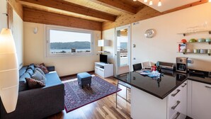 A modern kitchen with a central island, a dining area with a sofa and ottoman, and a large window offering a view. - Apartment 'Rocchetta' with Lake View, Wi-Fi and Air Conditioning (Salò)