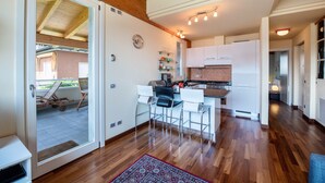 A modern kitchen with white cabinets, a dining area with white chairs, and a wooden ceiling. - Apartment 'Rocchetta' with Lake View, Wi-Fi and Air Conditioning (Salò)