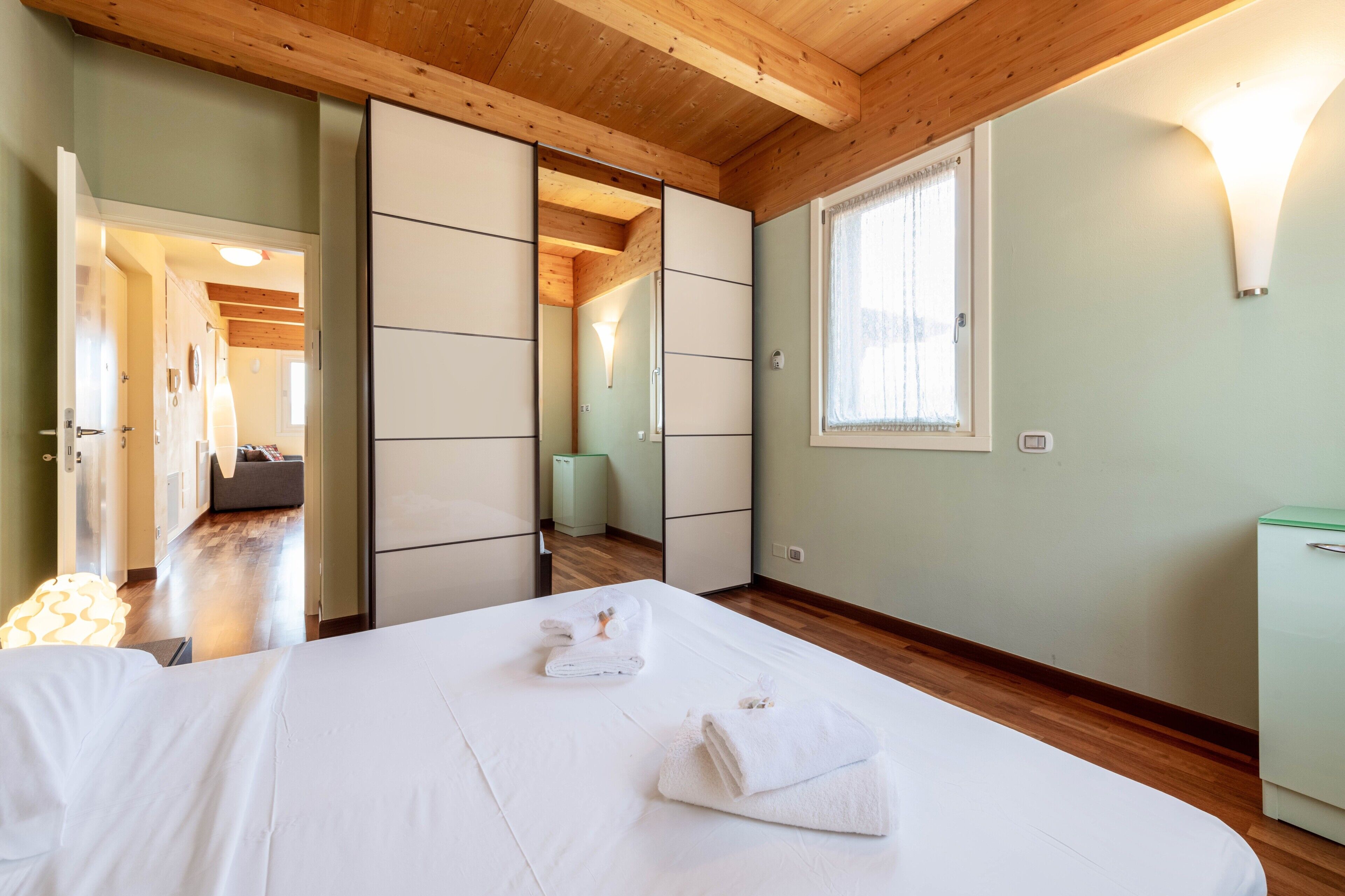Quarto de hotel com uma cama, guarda-roupa, janela e porta que dá para outro quarto.