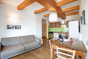 A modern living room with a sofa, wooden dining table, and kitchen in the background.