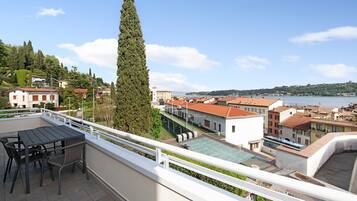 Un balcone con tavolo e sedie, affaccia su una cittadina con edifici e un corpo d'acqua.