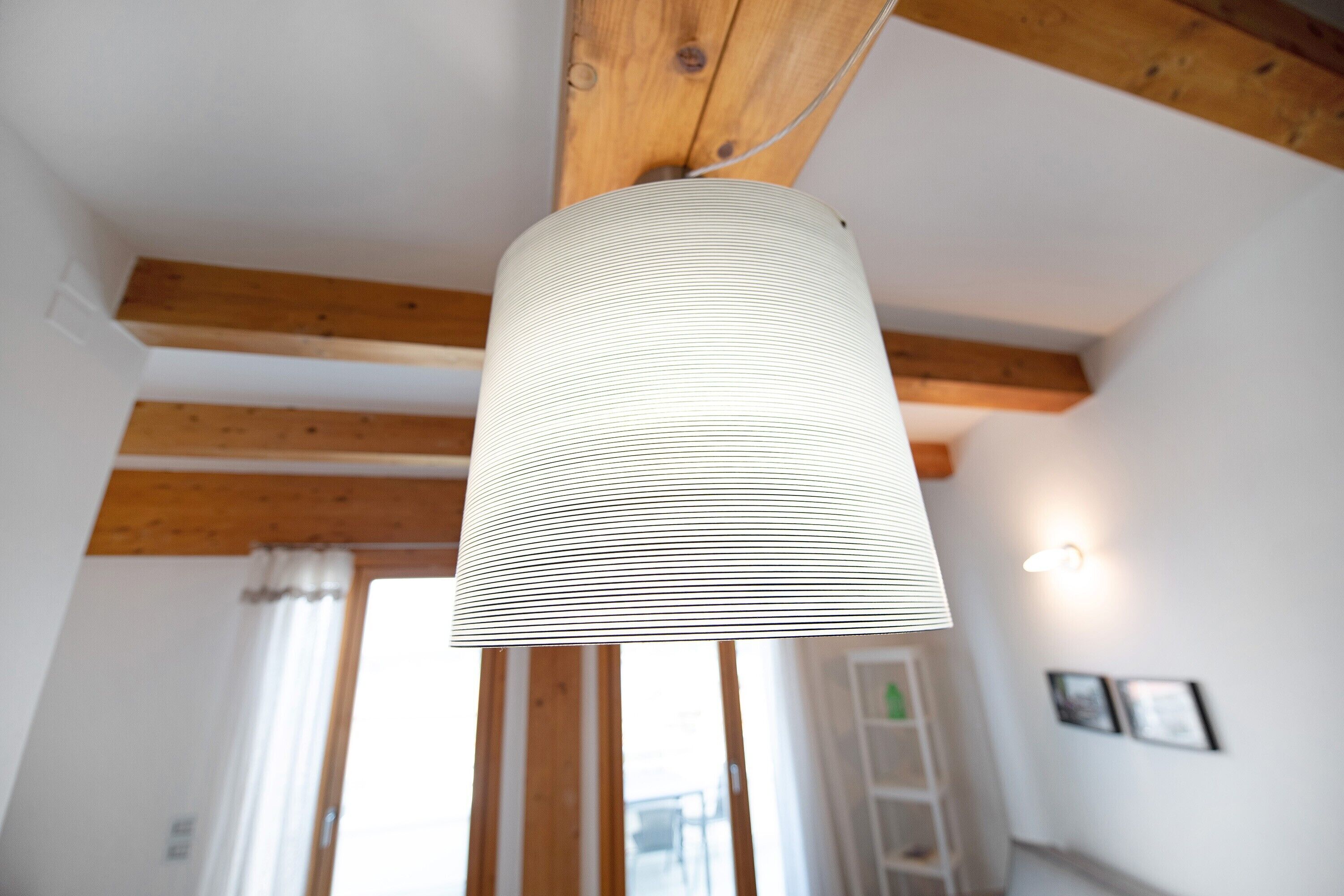 Habitación con vigas de madera a la vista, lámpara colgante, puerta con cortina y luz empotrada en la pared.