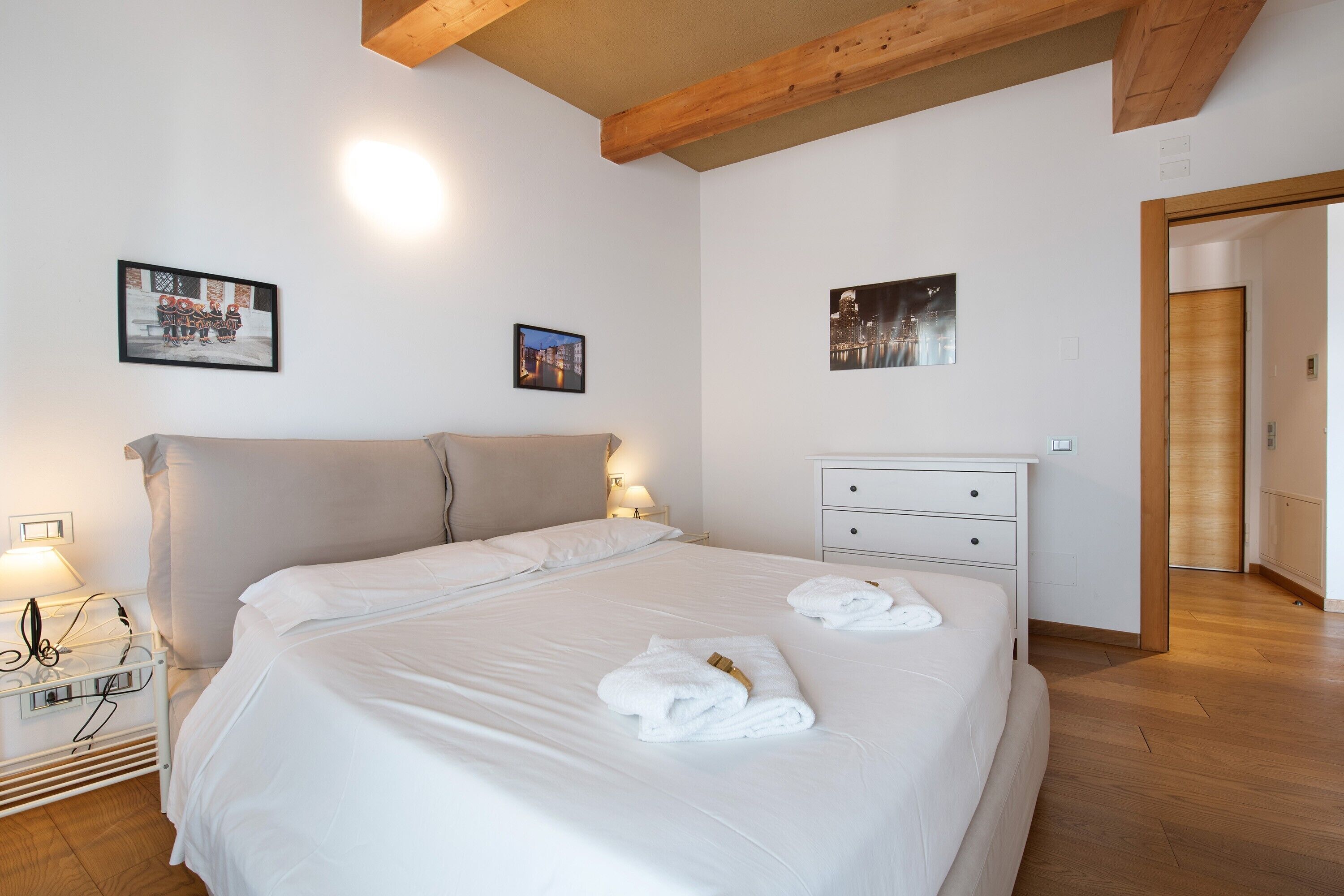A hotel room with a bed, bedside tables, a nightstand, a wooden ceiling, and two wall-mounted pictures.