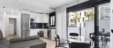 A modern apartment with a living area, kitchen, and balcony with a view of buildings.