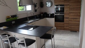Une cuisine moderne dotée d’un îlot central, d’appareils électroménagers en acier inoxydable et d’une fenêtre laissant entrer la lumière naturelle.