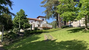 Un bâtiment à deux étages, surmonté d’un toit recouvert de tuiles rouges, entouré d’une végétation luxuriante et d’arbres.