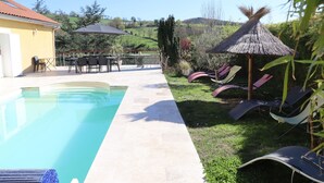 Une piscine avec un espace patio, des chaises longues et un parasol en chaume.