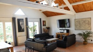 Un salon spacieux avec un plafond haut, un grand téléviseur et un coin repas comprenant une table et des chaises.