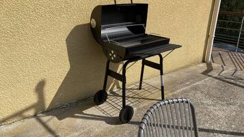 Un barbecue portable adossé à un mur texturé, avec une chaise en métal devant.